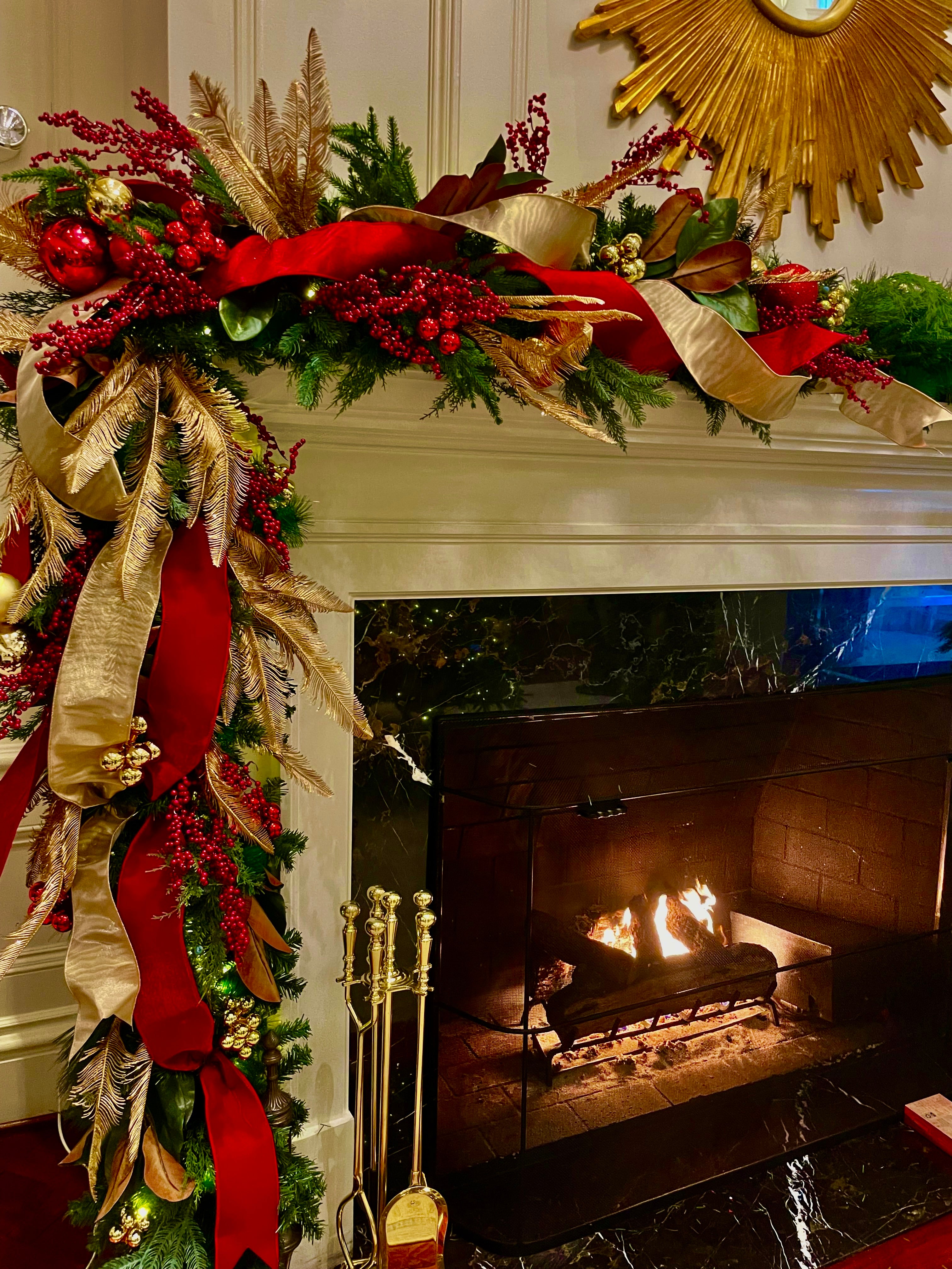 Decorative Christmas mantel with garland and ribbons over a fireplace.